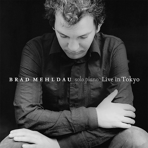 Black and white photo of Brad Mehlauf sitting with his arms crossed, looking down, with text overlay: 'Brad Mehlauf solo piano Live in Tokyo'.